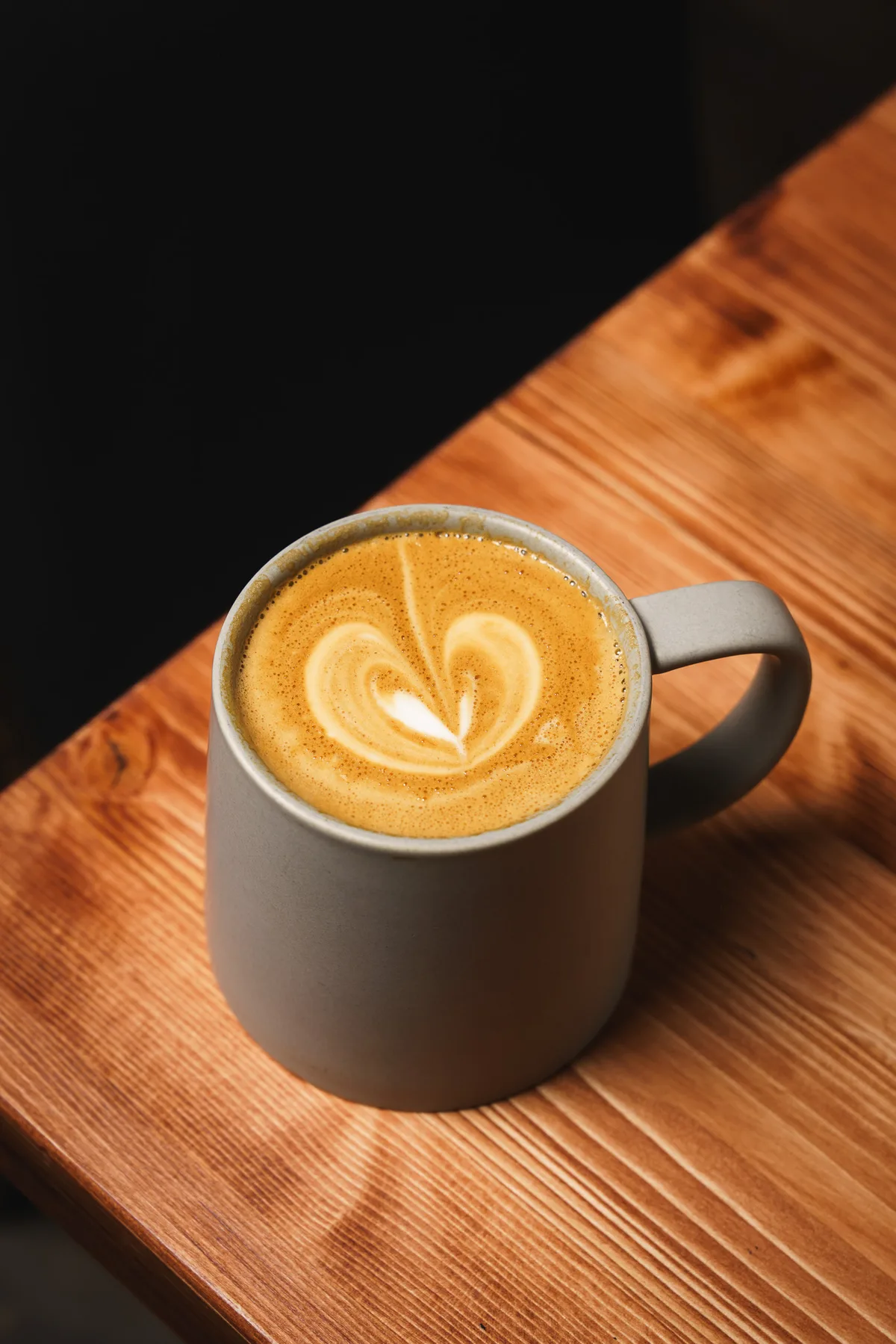 Latte with heart latte art in a gray mug on a wood table at Spotlight Café & Creamery